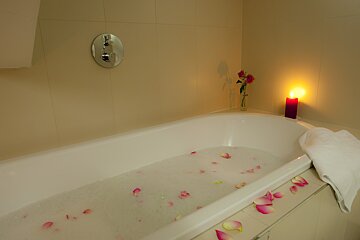 A bathtub filled with water and rose petals next to a candle