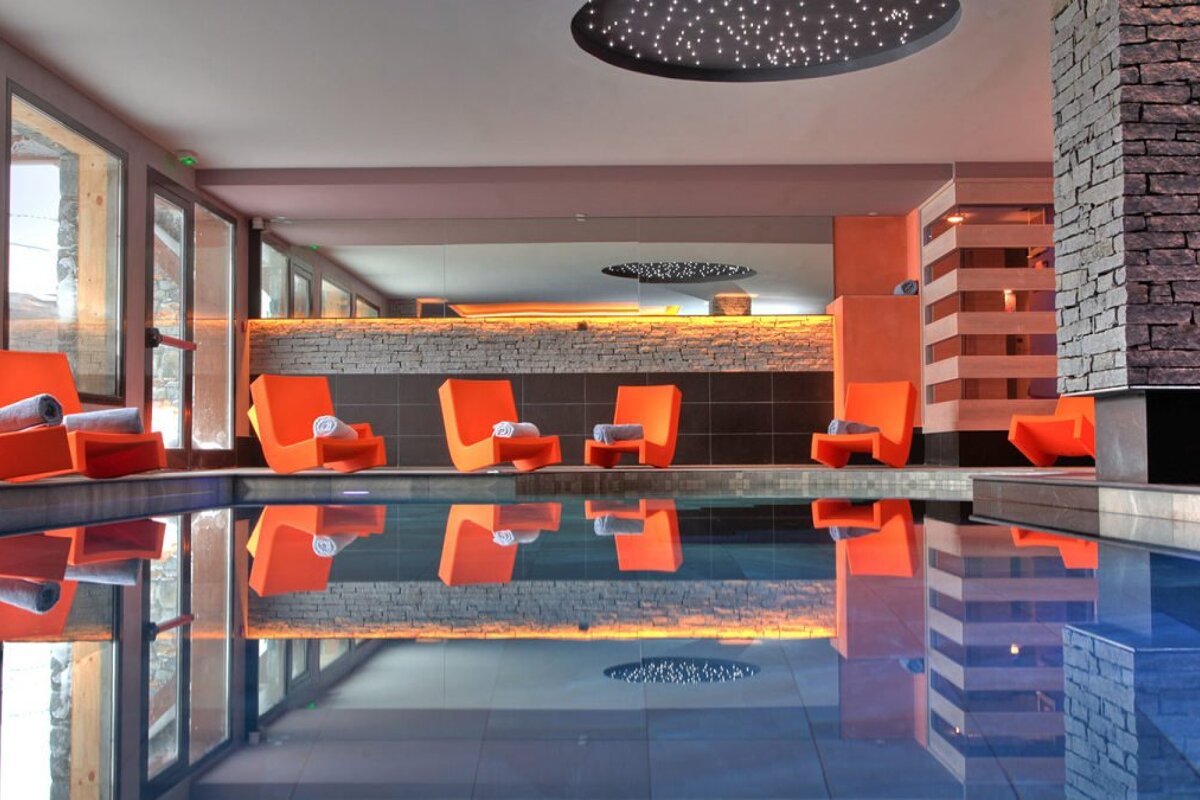 an indoor swimming pool with orange chairs around the sides