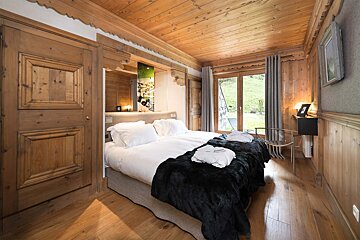 A wooden bedroom with two beds and a chair