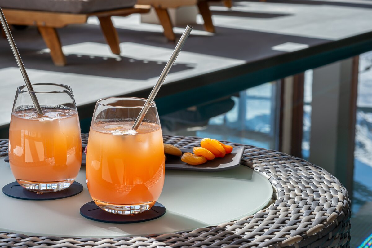 Two glasses of orange juice with straws on a wicker table