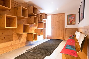 A rustic wooden ski chalet entryway features floating cube shelves, a warm wooden door, a 