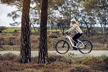 A woman wearing a helmet is riding an electric bike on a road