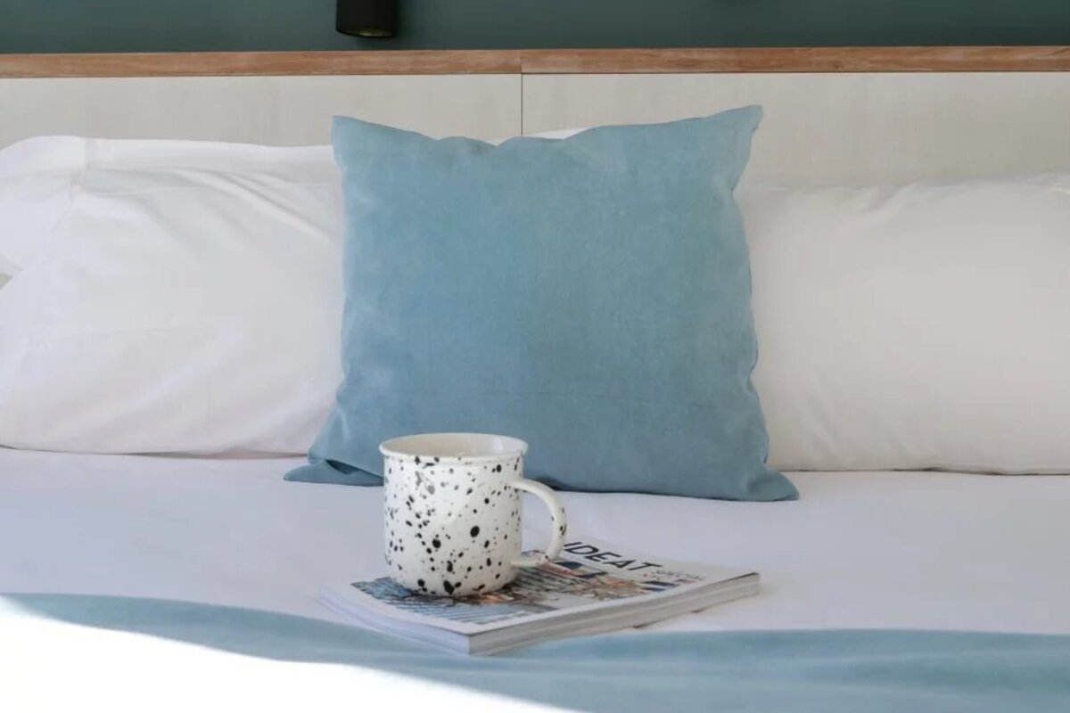 A bed with a blue pillow and a mug on it