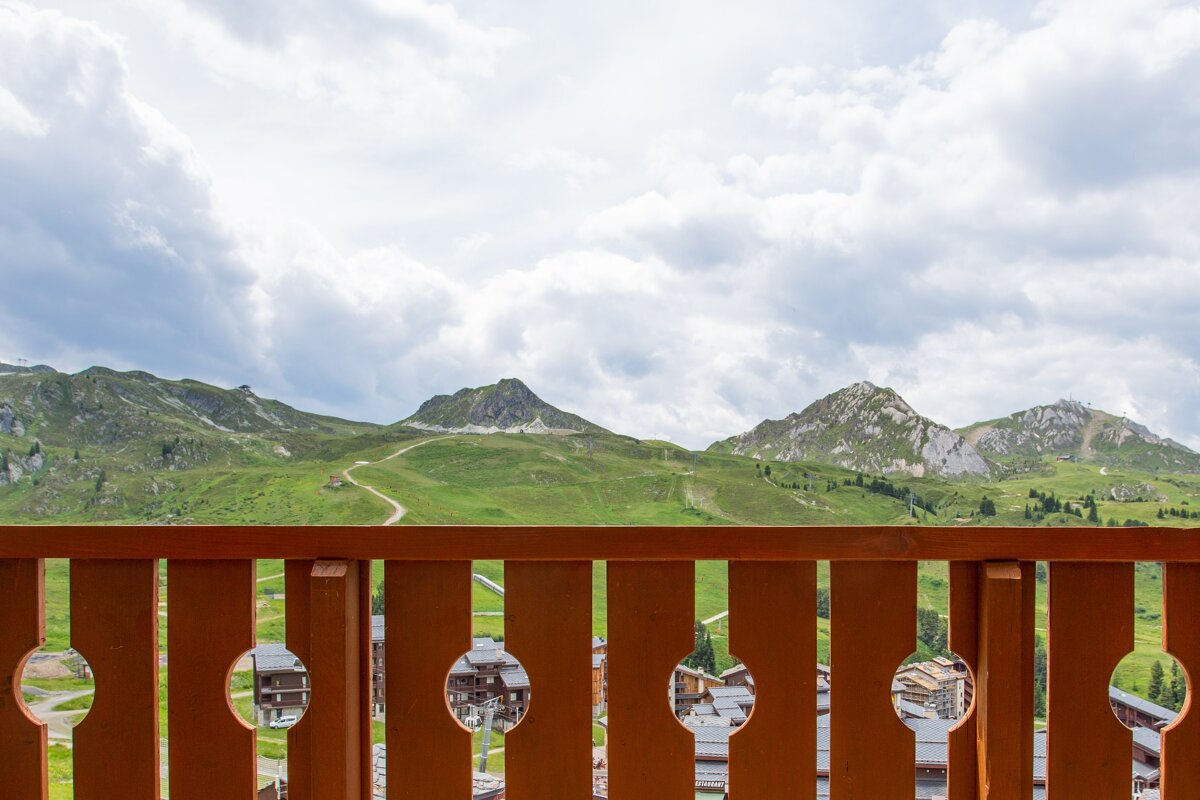 A view of a mountain range from a balcony with a wooden railing