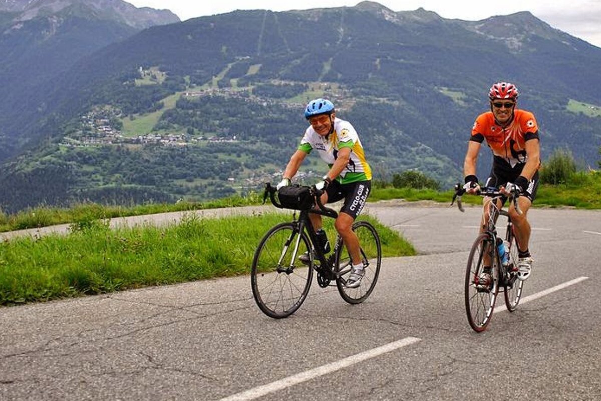 Two men are riding bicycles down a road with mountains in the background