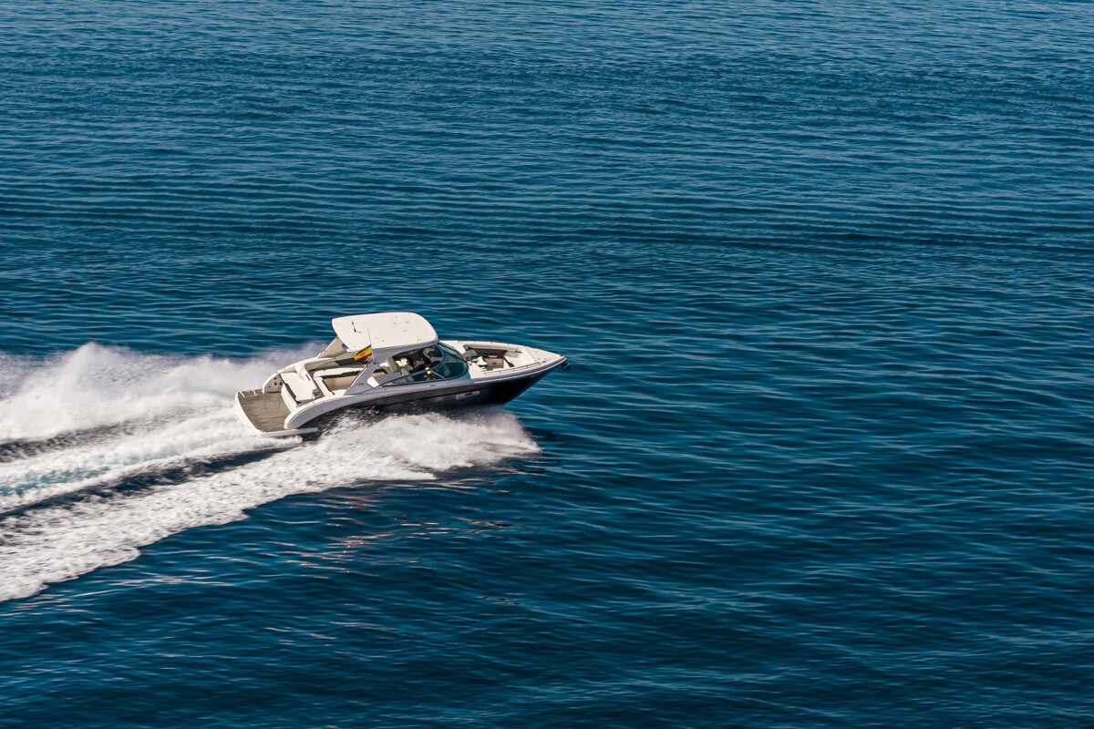A white motorboat speeds across the deep blue ocean, leaving a white wake behind it.
