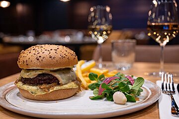 A hamburger and french fries on a plate with a glass of wine in the background