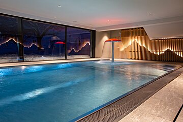 Modern indoor pool featuring a red mushroom fountain, large windows revealing a snowy outdoor night scene, and illuminated wooden slat wall decor.