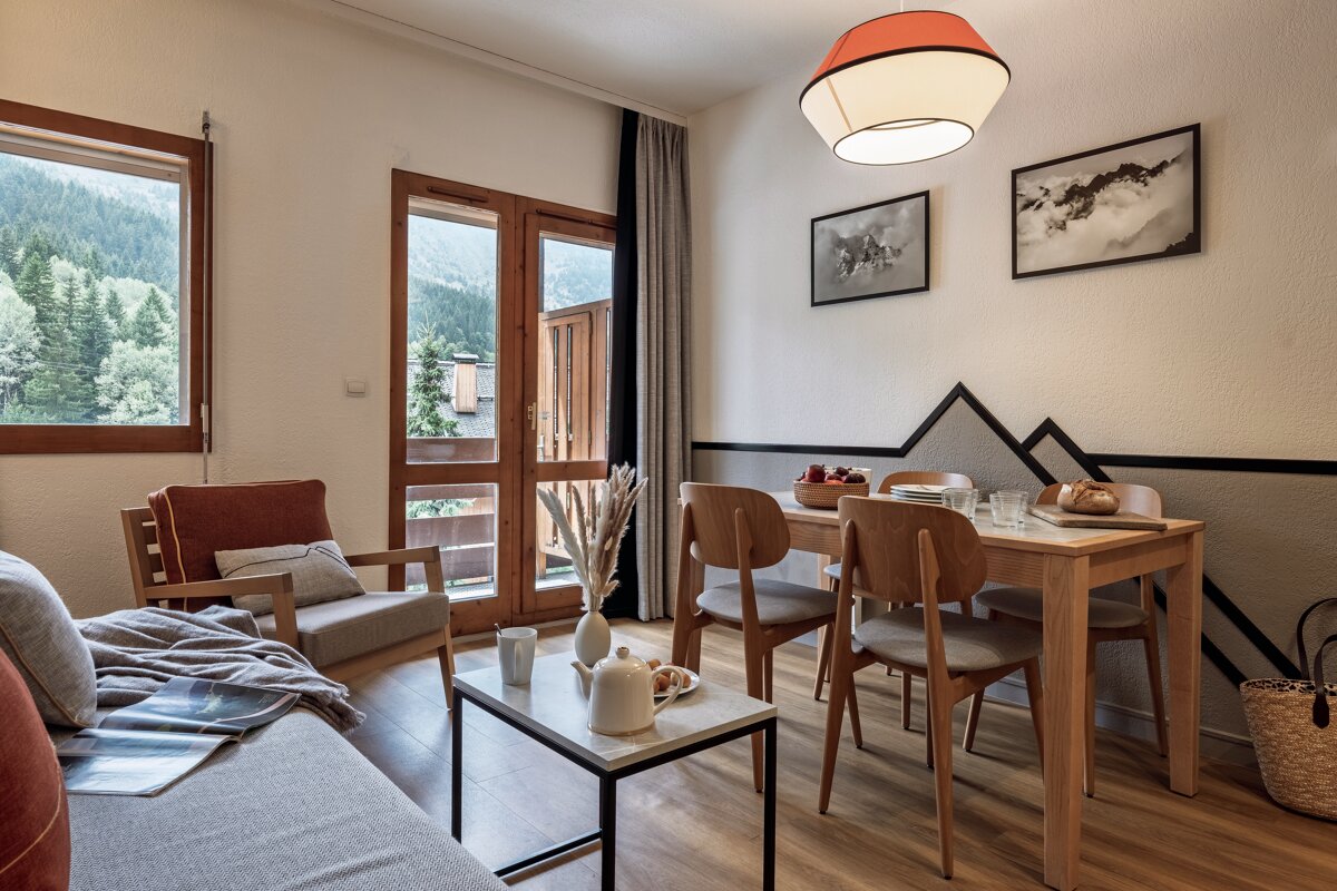Cozy cabin interior featuring a wooden dining set, living area with coffee table, and scenic mountain views through the windows.