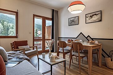 Cozy cabin interior featuring a wooden dining set, living area with coffee table, and scenic mountain views through the windows.
