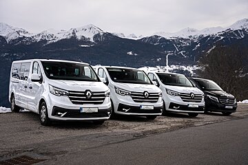 A row of white vans are parked in front of snowy mountains