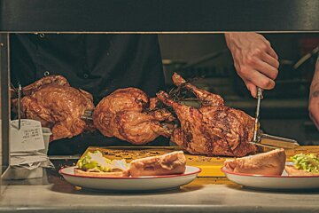 A person is cutting a roasted chicken with a pair of scissors
