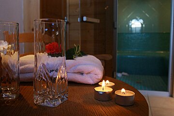 A glass with a rose in it sits on a table next to candles