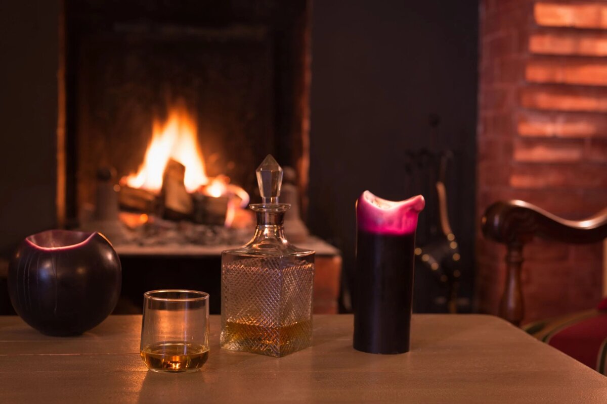 A glass of whiskey sits on a table in front of a fireplace