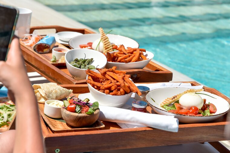 A person is taking a picture of a tray of food by a pool