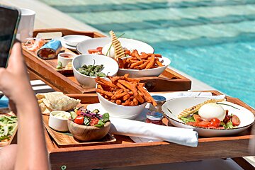 A person is taking a picture of a tray of food by a pool