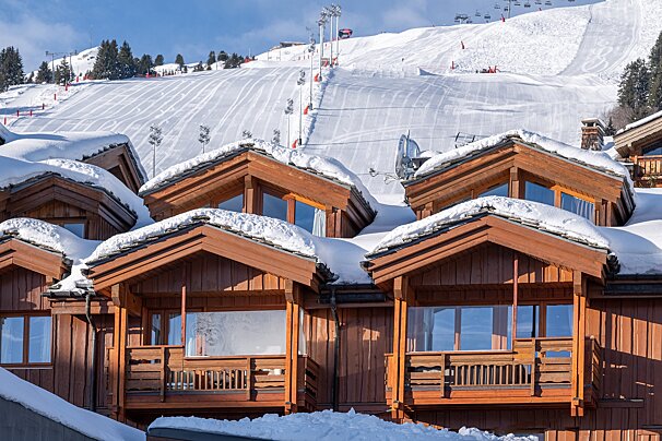 A row of wooden houses covered in snow with a ski slope in the background