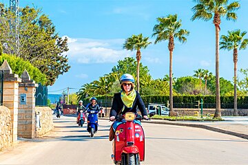 A woman wearing a yellow scarf is riding a red scooter