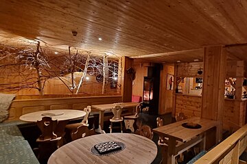 A cozy, rustic wooden dining room with decorative bare trees, warm lighting, wooden tables, chairs, benches, and a glowing fireplace.