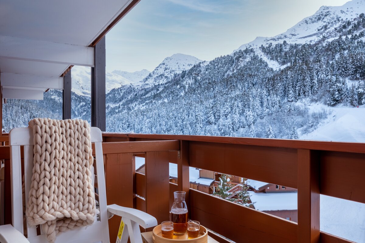 A bottle of beer sits on a tray on a balcony overlooking snowy mountains