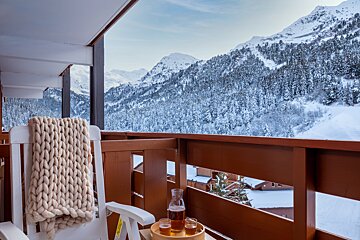 A bottle of beer sits on a tray on a balcony overlooking snowy mountains