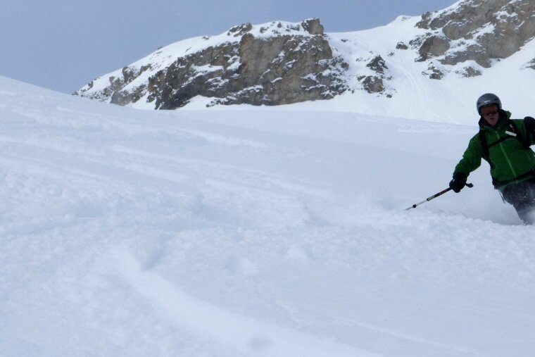 A man in a green jacket is skiing down a snowy slope