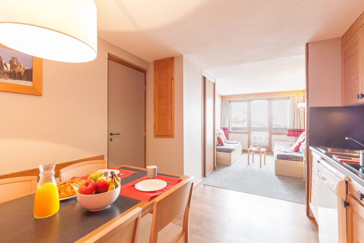 A bowl of fruit sits on a table next to a pitcher of orange juice