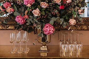 A vase filled with pink flowers sits on a table next to wine glasses