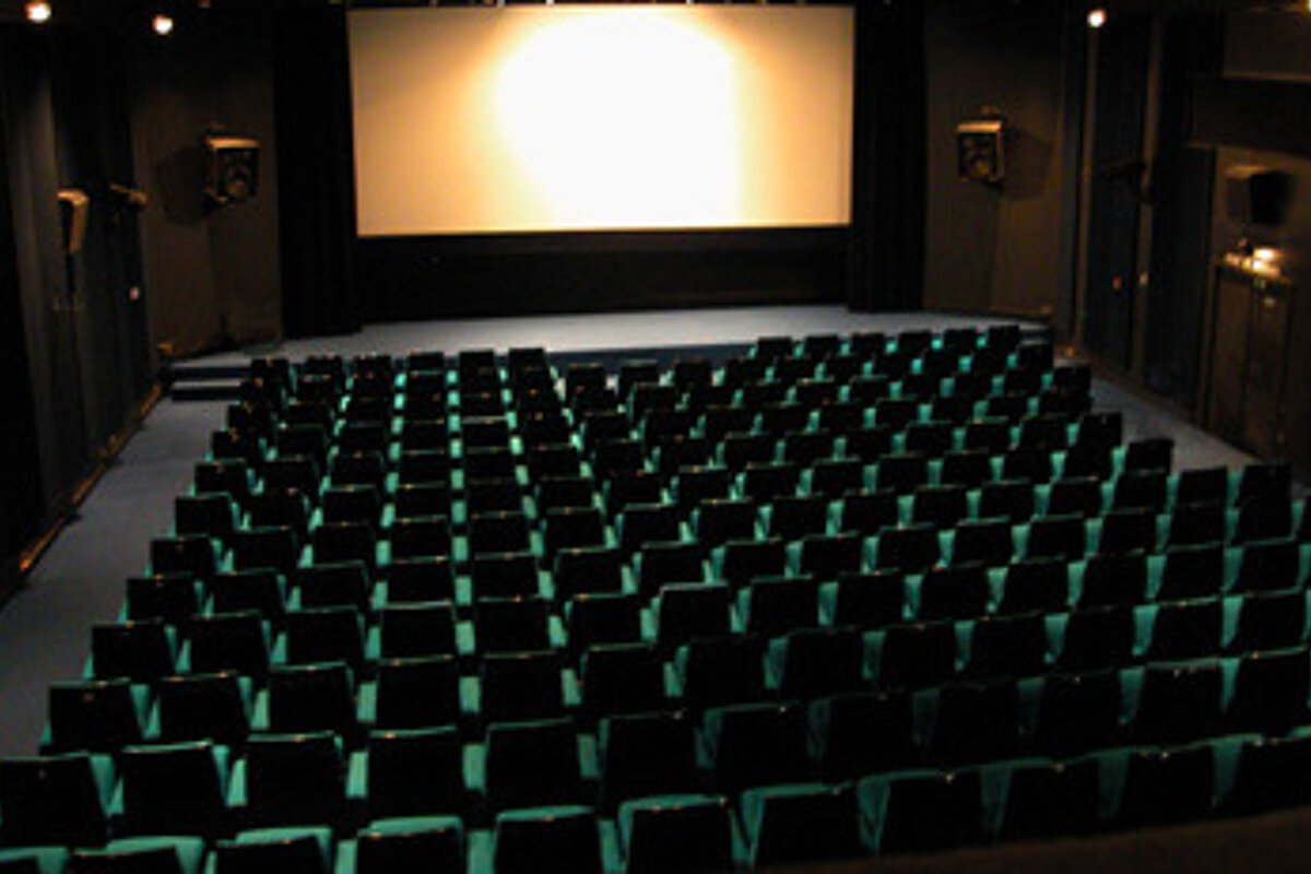 An empty movie theater with green seats and a large screen