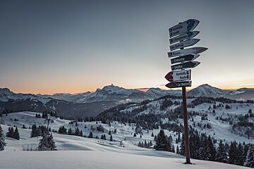 Sunset over the mountains in Les Gets with snow and a signpost in the foreground