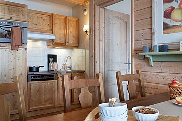 A cozy rustic cabin kitchen and dining area with wooden cabinetry, chairs, and a table set with breakfast bowls.