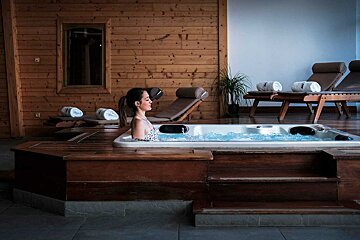 A woman sits in a hot tub surrounded by chairs and towels
