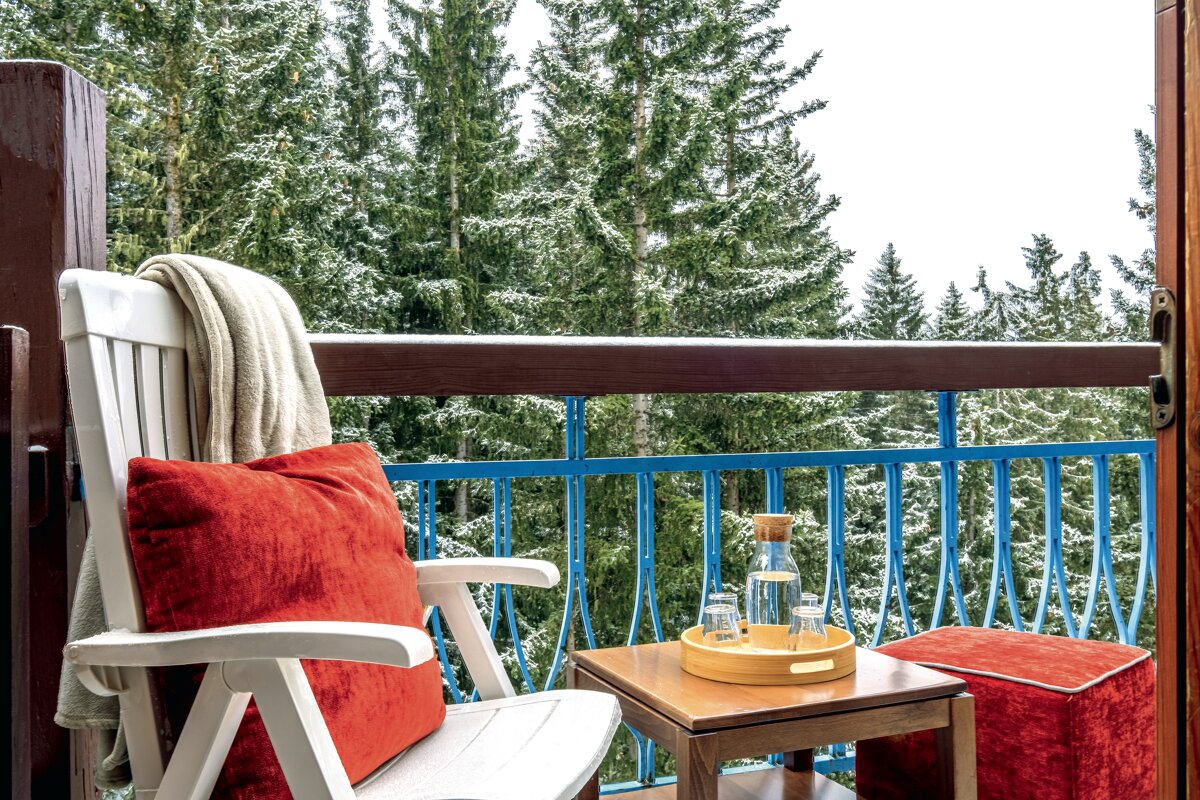 A chair with a red pillow sits on a balcony overlooking a snowy forest