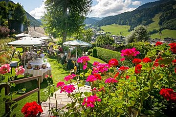 People sitting at tables in a garden surrounded by flowers and umbrellas