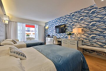 A hotel room with two beds a desk and a flat screen tv