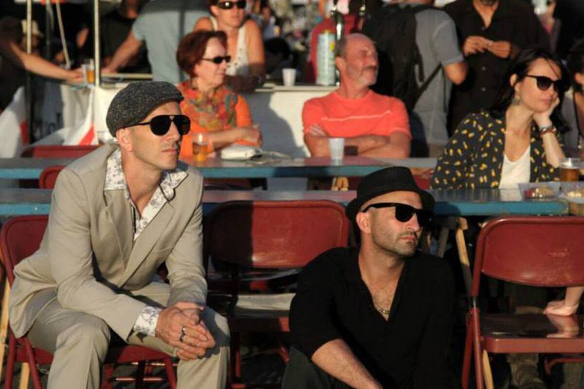 2 men with hats and sunglasses watching music at sunset