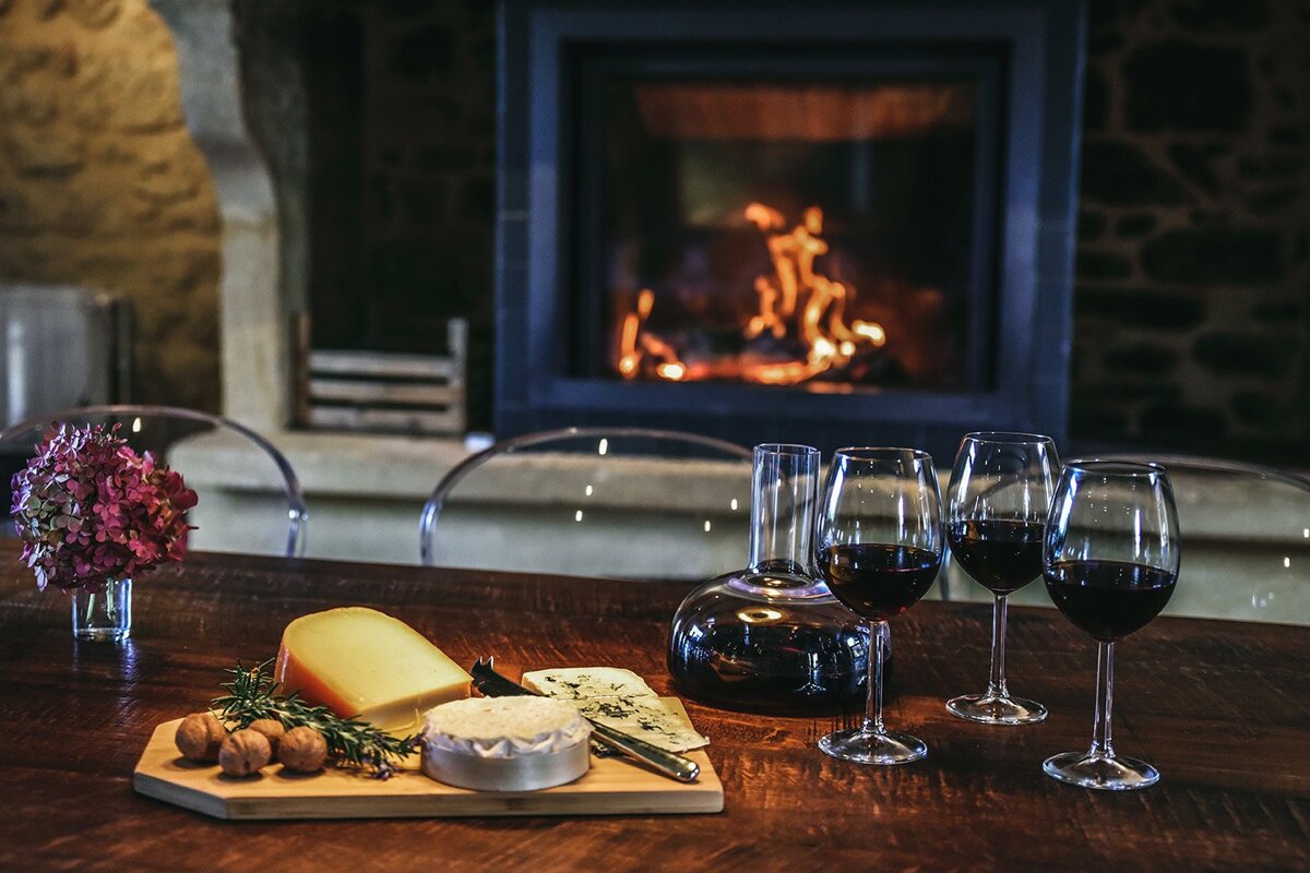 Two glasses of wine sit on a table in front of a fireplace
