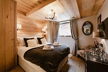 A warm, wood-paneled bedroom with a large bed, antler chandelier, and rustic decor, offering a cozy, chalet-style ambiance.
