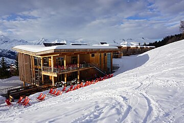 A row of red chairs sit in front of a snow covered building