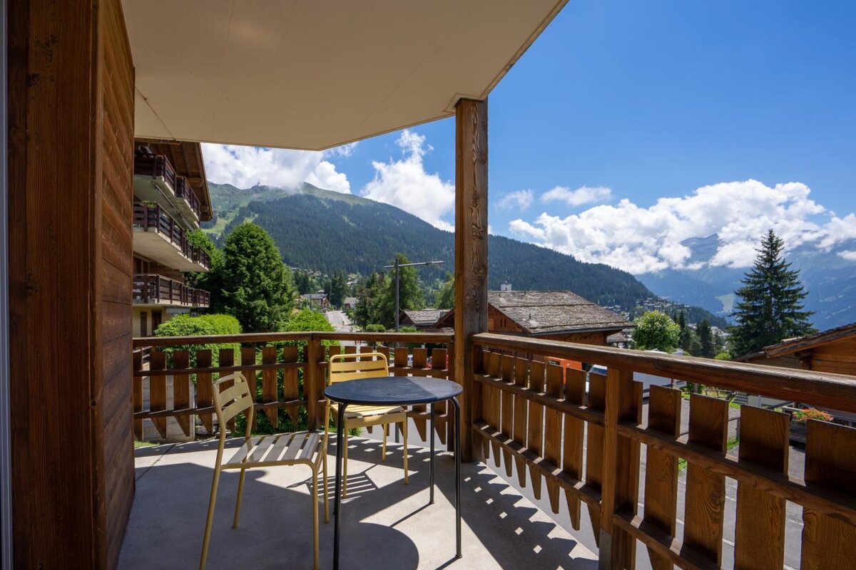 A balcony with a table and chairs and mountains in the background