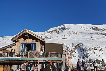 A group of people standing outside of a building with a mountain in the background