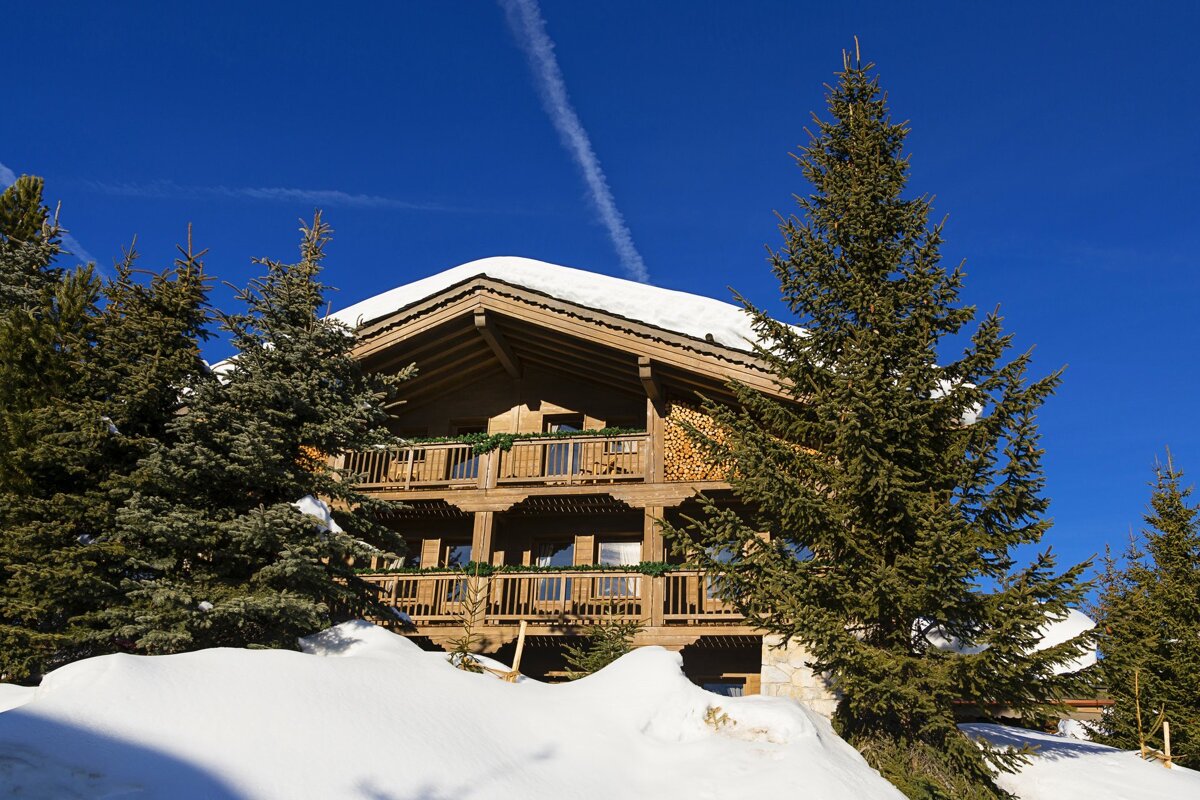 A large wooden house is surrounded by snow covered trees