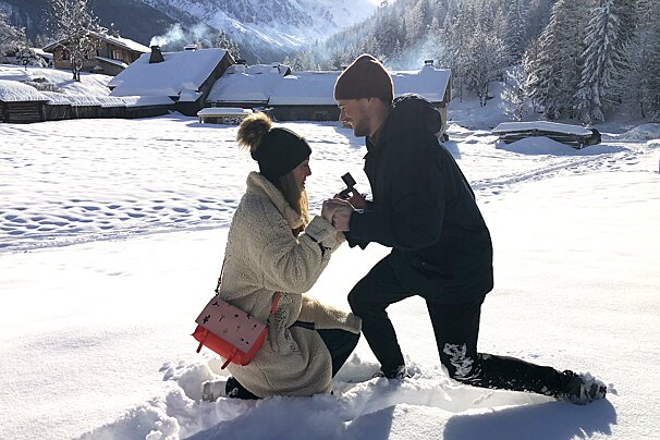 A man kneeling down to propose to a woman in the snow