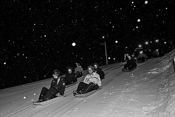 A group of people sledding down a snowy hill at night