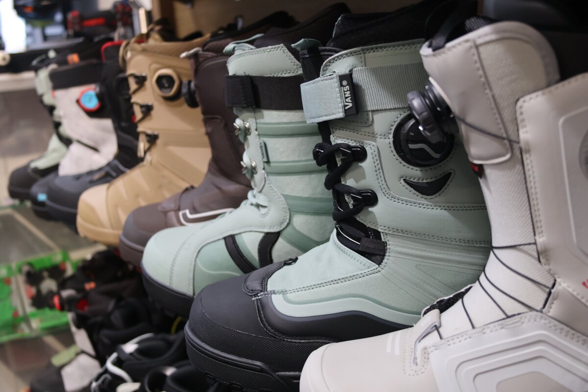 A close-up shot of several pairs of snowboard boots, including mint green Vans, lined up on display in a store.