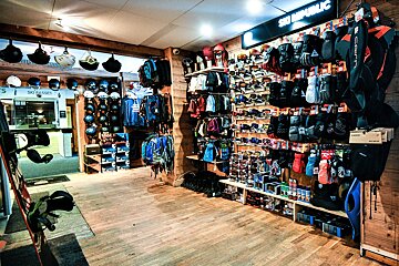 An indoor ski and snowboard shop with a wide selection of helmets, goggles, gloves, and apparel displayed on wooden fixtures.