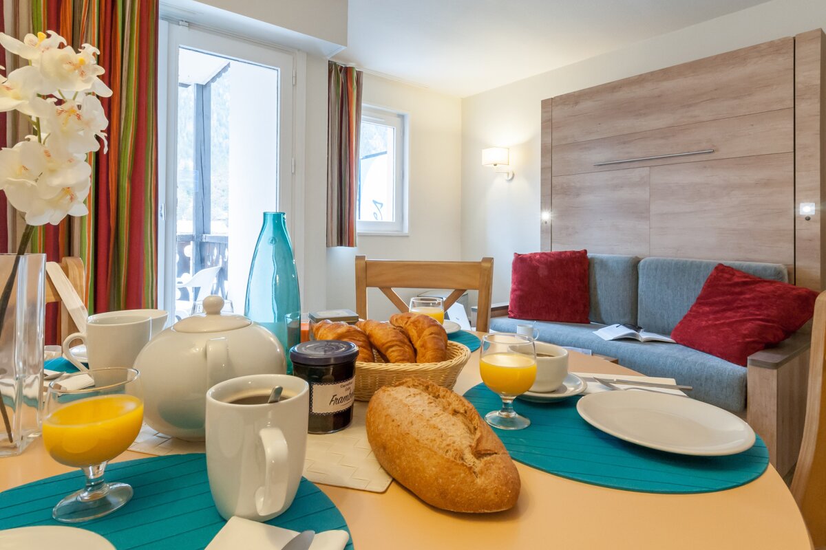 A jar of jam sits on a table next to a loaf of bread