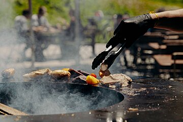 A person wearing black gloves is holding tongs over a pot of food