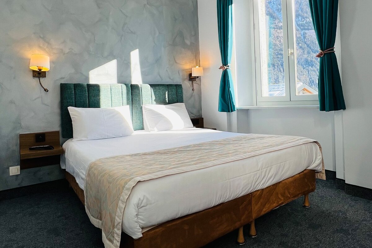 A hotel room with a large bed and green chairs