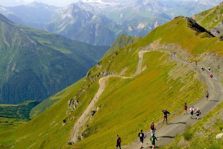 A group of people are walking down a dirt road in the mountains